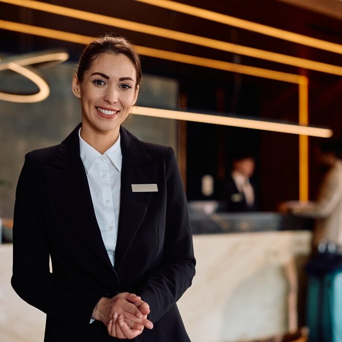 Smiling,Female,Hotel,Receptionist,In,A,Hallway,Looking,At,Camera.